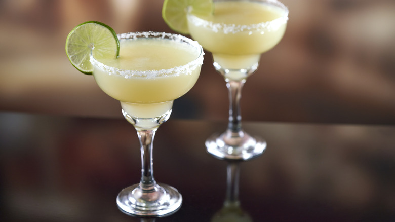 Two margaritas with lime wheels in stem glasses