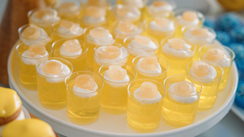 A tray of yellow Jell-O shots with cream on top of them.