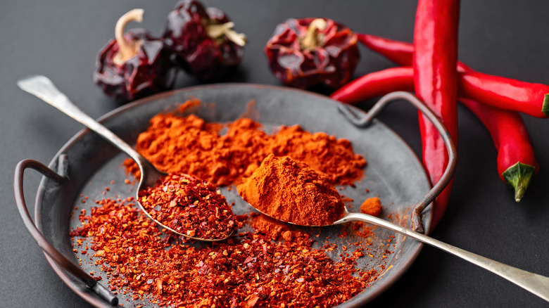 Spicy red chili peppers, chili powder, and Spanish paprika with drried chipotle peppers in the background