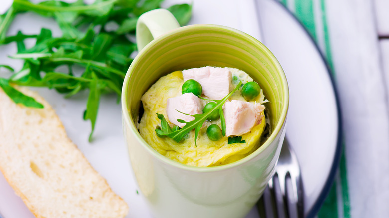 microwaved eggs in coffee cup next to greens and slice of bread