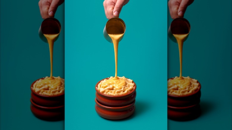 Pouring melted cheddar cheese onto macaroni and cheese in a small dish