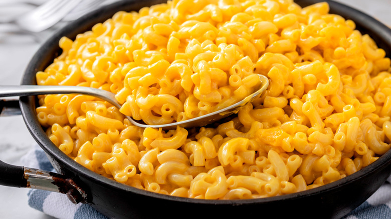 A pot of orange mac and cheese with a serving spoon and kitchen towel