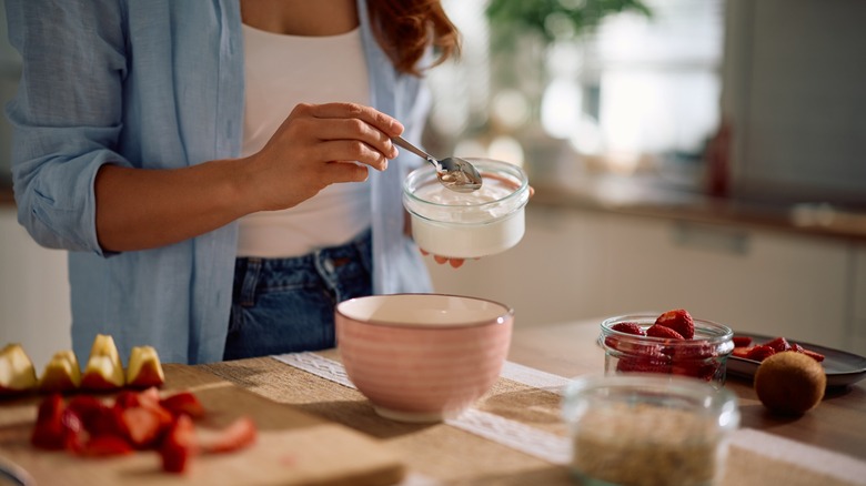 Close up of a woman spooning Greek yogurt into a bowl while making oatmeal at home