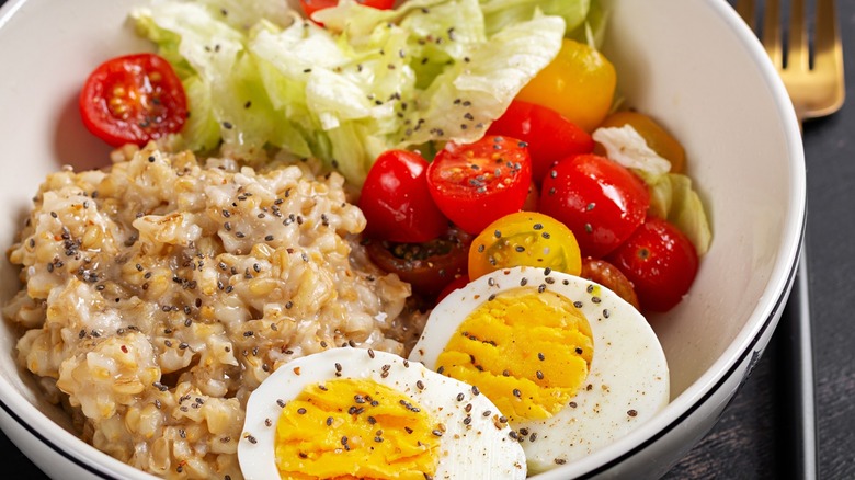 A bowl of savory oatmeal with fresh salad and a boiled egg