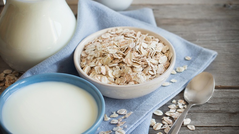 Rolled oats in a bowl next to a bowl of milk on a wooden table