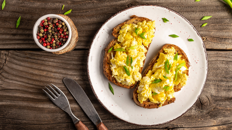 Scrambled eggs on wheat toast with green onions and bowl of peppercorns