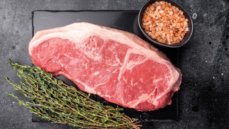 A steak next to seasoning salt and sprigs of thyme