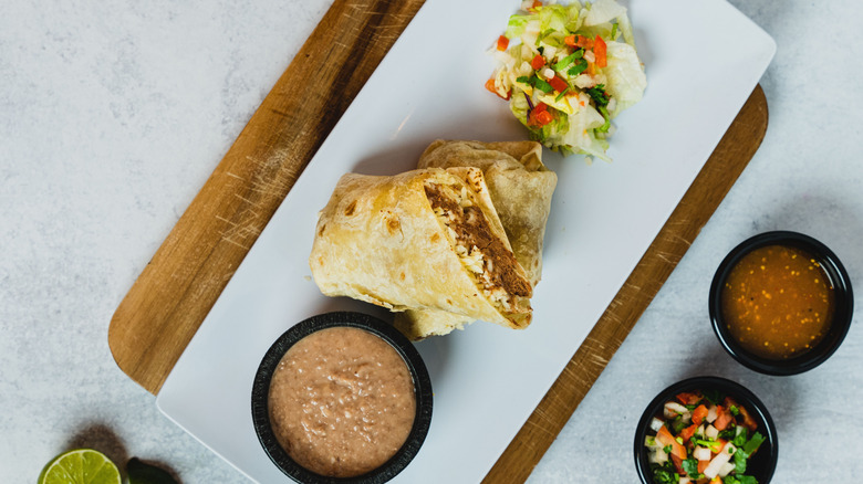 A burrito with refried beans on the side