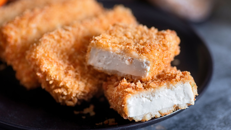 rectangles of crispy breaded tofu next to each other with the first one cut in half, exposing it's interior