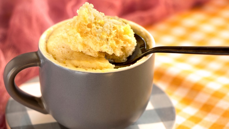 Close up of a vanilla mug cake with a spoon dipped in, all on patterned materials.