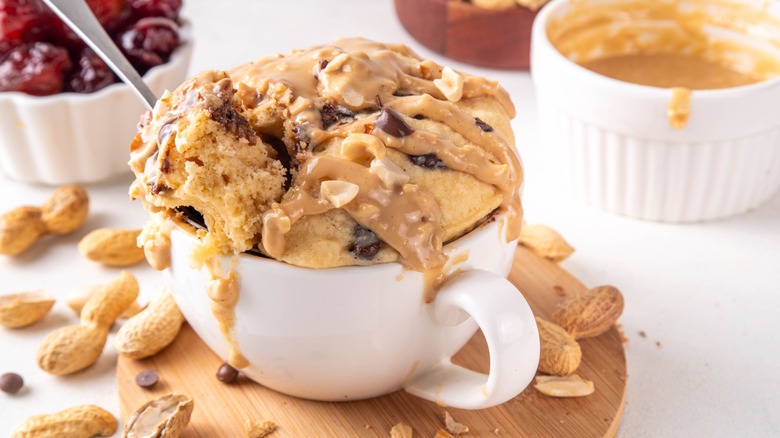 Close up of a peanut butter and chocolate mug cake with additional ingredients surrounding.