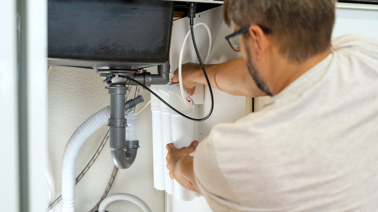 Plumber performs water filter maintenance under the kitchen sink