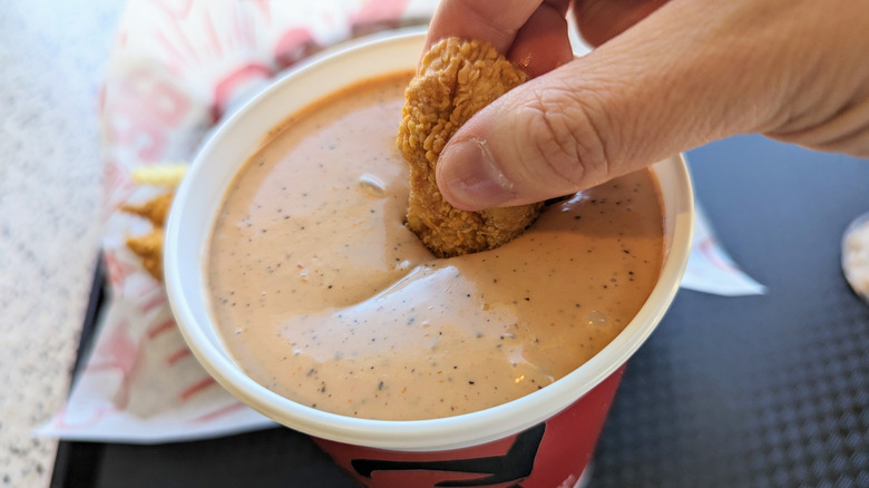 hand dipping tender in cup of sauce