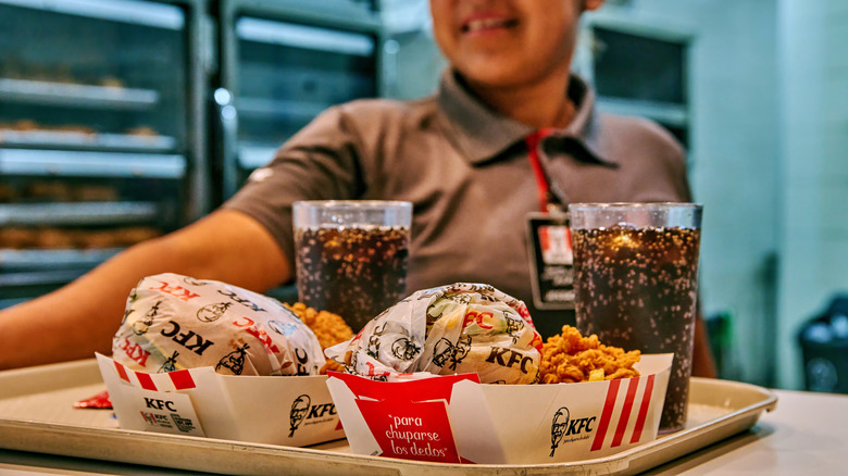 An employee sets out a plastic tray of KFC food, including sandwiches and drinks.