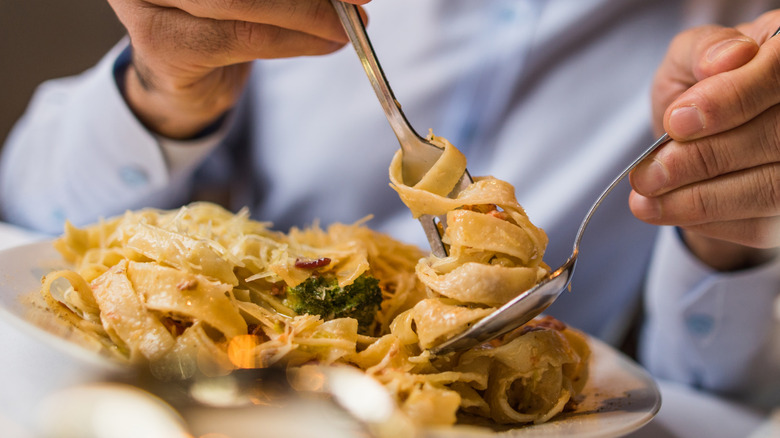 Person eating fettuccine Alfredo with fork and spoon