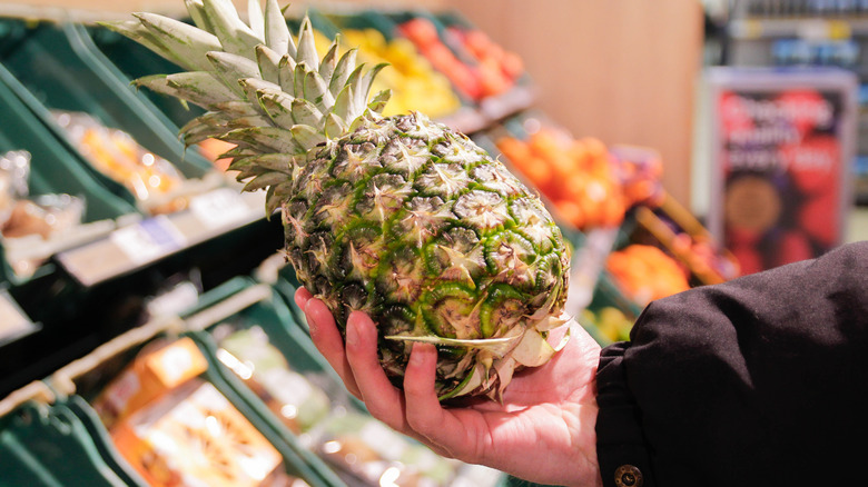 A person holding a pineapple in a grocery store