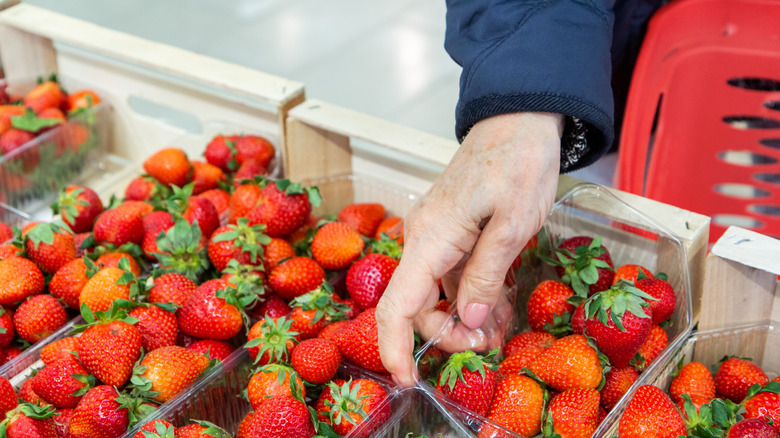 hands shop for containers of strawberries in store