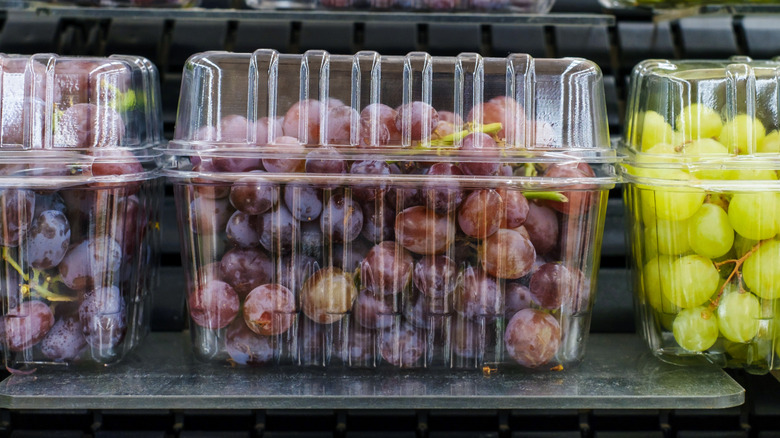 Green and red grapes in plastic clamshell packages on grocery store shelf