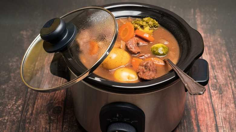 Small slow cooker filled with beef and veggies on a wooden table