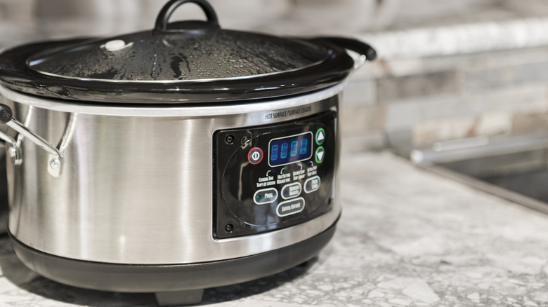 A slow cooker on a granite countertop warms food on a low setting