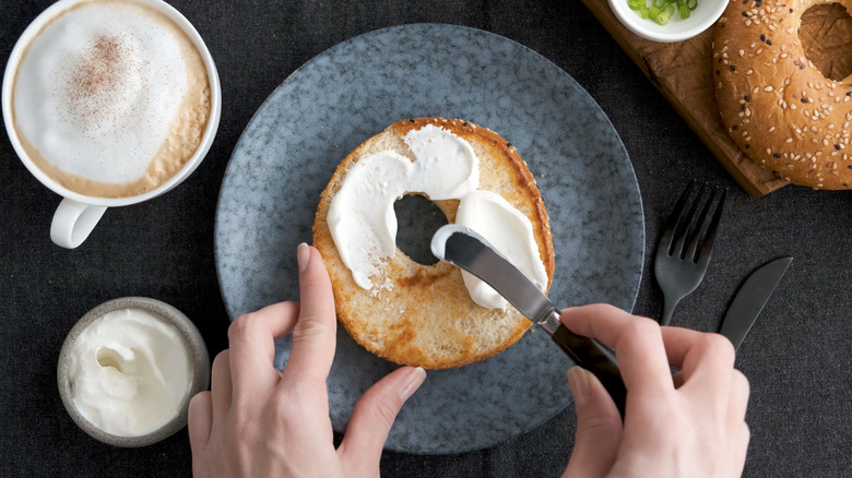 Top view of hands spreading cream cheese on toasted bagel