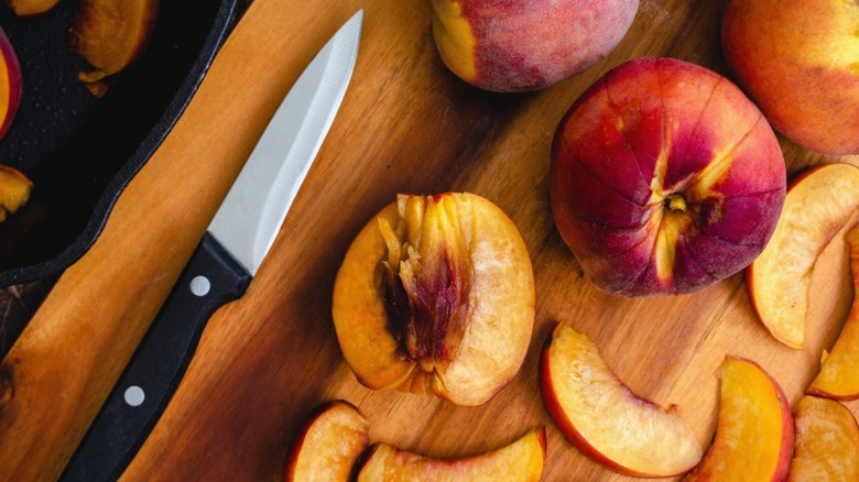 Several peaches on a cutting board next to a knife.