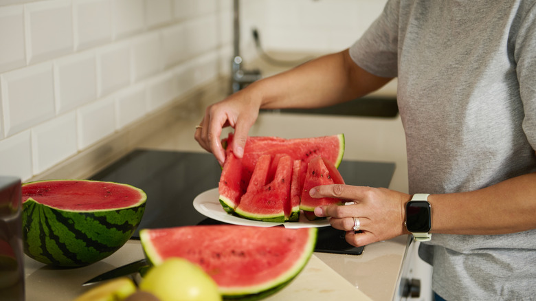Person putting cut-up watermelon on a plate on a kitchen counter