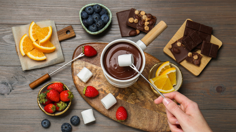 Melted chocolate in a white dish with marshmallows and fruits for dipping