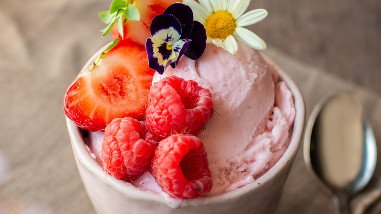A bowl of strawberry frozen yogurt with fresh berries and flowers