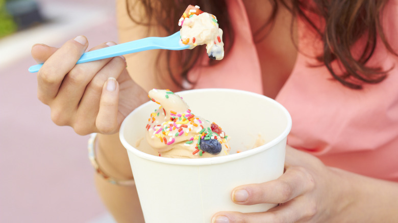 A woman eats frozen yogurt topped with fruit and sprinkles