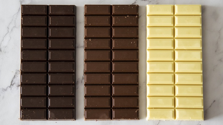 Dark, milk, and white blocks of chocolate sitting on a counter.
