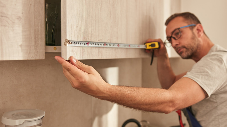 A person measuring a kitchen cabinet.