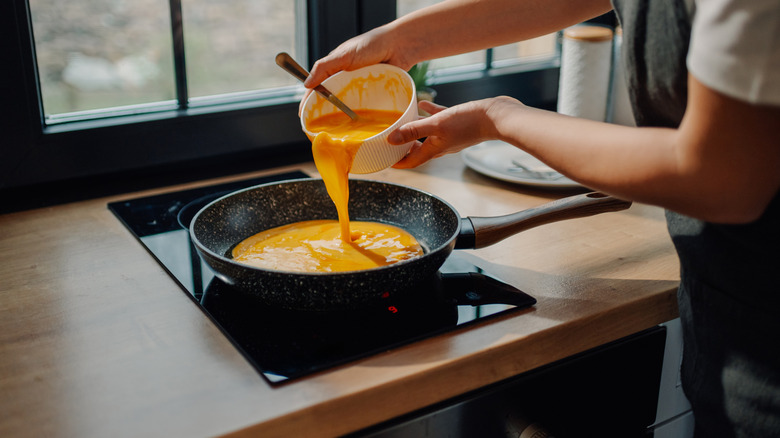 Chef pouring cheese sauce into a pan on a induction stove