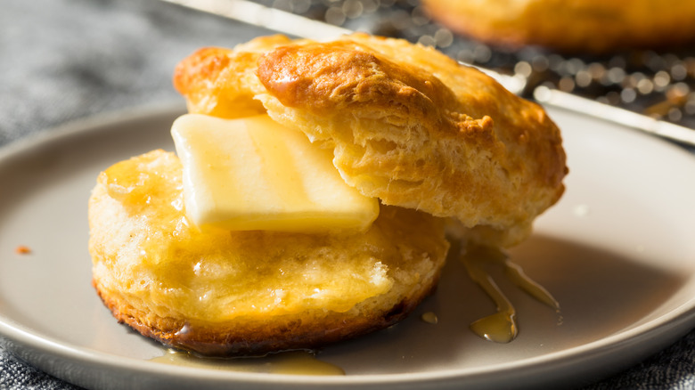 A warm biscuit with a pat of butter and honey on a plate