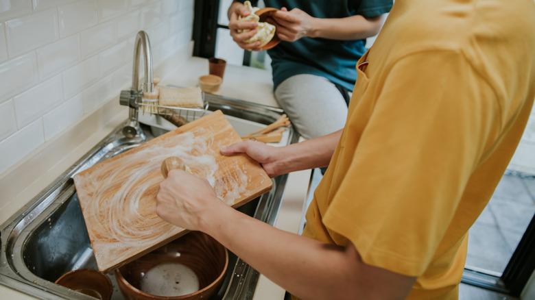A person in an orange shirt washing a wooden serving board with soap and water