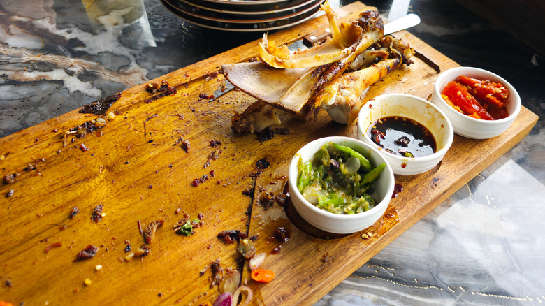 A wooden serving board with bones, food residue, and bowls of garnish