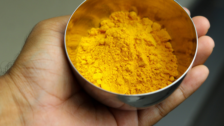 hand holding metal bowl of golden turmeric powder