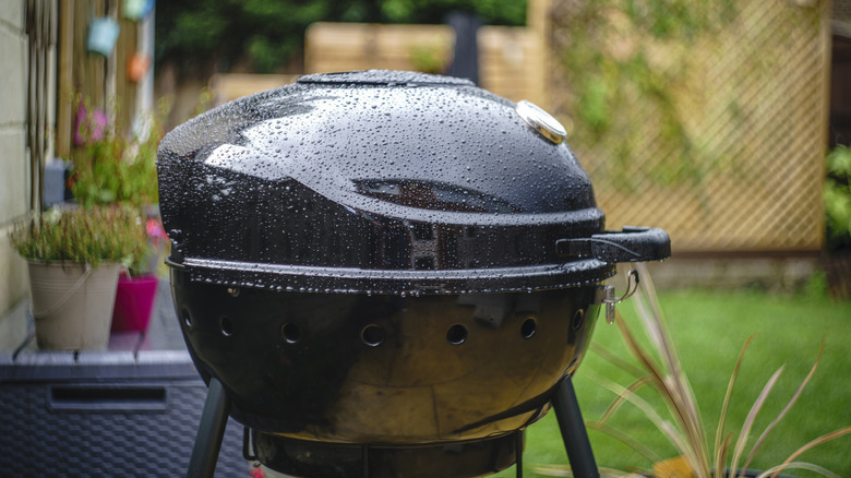 Rain droplets dot a black outdoor grill in a yard
