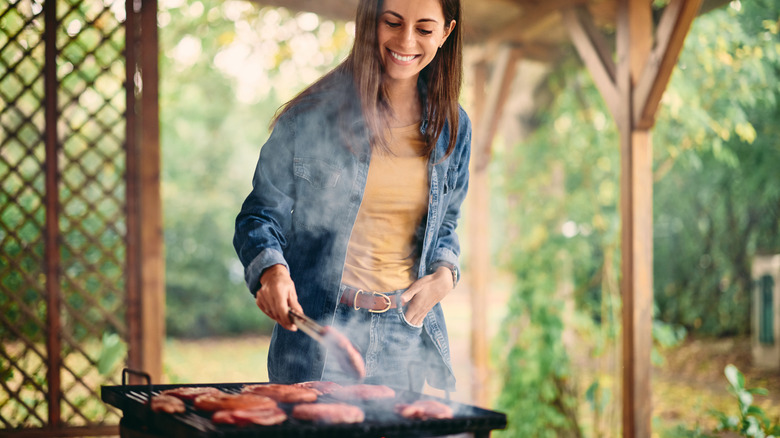 A woman grills outside under a large wooden gazebo