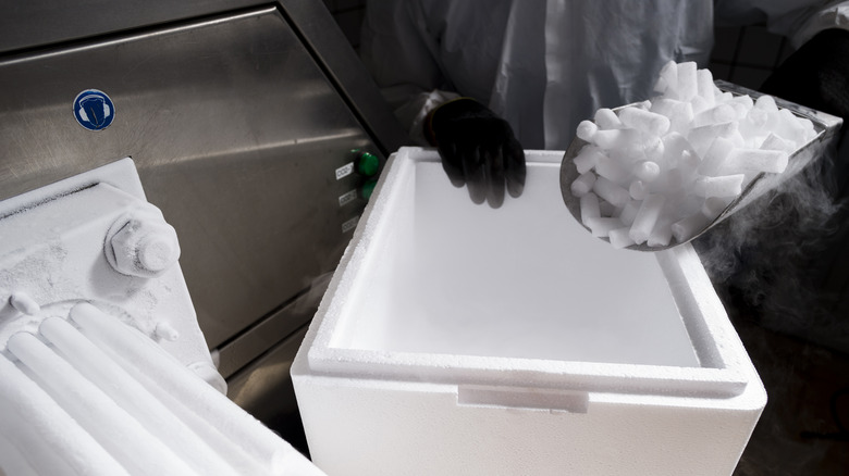 gloved hand holding scoop of dry ice above cooler