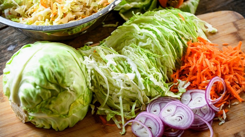 Shredded cabbage, red onions, and carrots on wood cutting board