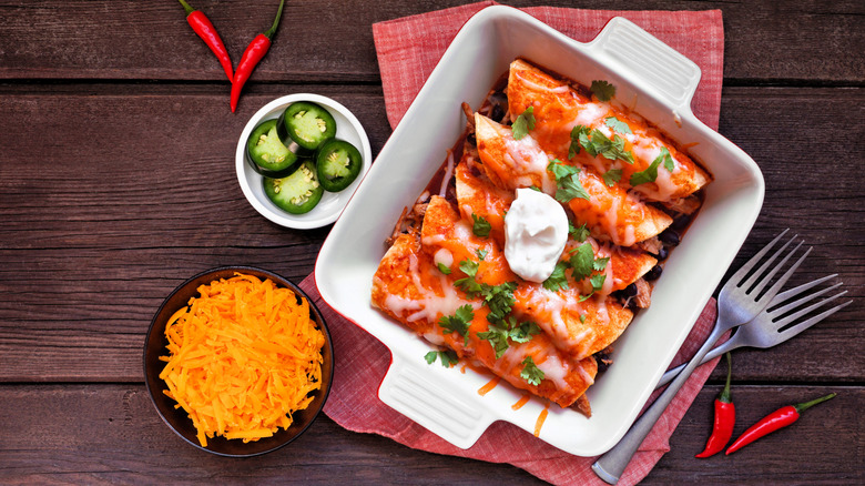 Red enchiladas in a white dish with jalapeños and cheese
