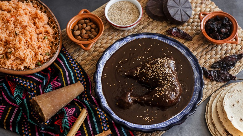 Chicken with mole sauce with small bowls of seasonings and rice