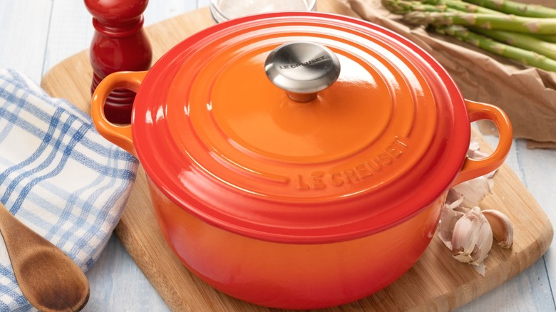 An orange Le Creuset Dutch oven on a wooden cutting board