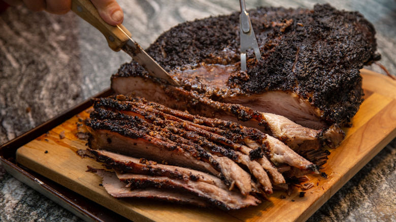 Smoked brisket being sliced on a wooden board