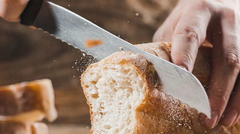 A person slicing bread with a serrated knife