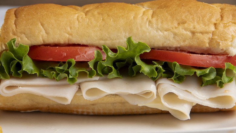 A sub sandwich with turkey, lettuce, and tomatoes on white bread