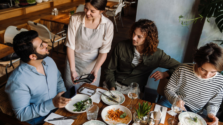 A man paying for his party's dinner at a restaurant using his smartphone.