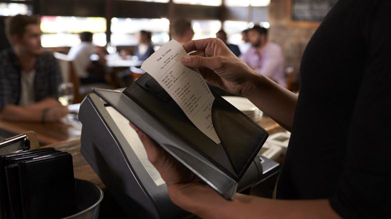 A waiter getting ready to hand the dinner bill to diners at a restaurant.