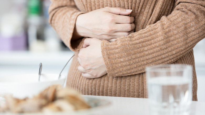 Person grabbing onto their stomach in front of a plate of food and glass of water